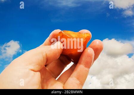 Orange dans la main avec une réflexion vive sur la paume contre le fond de la mer. Lumière vive de la pierre solaire dans la main femelle. Minéral de RE Banque D'Images