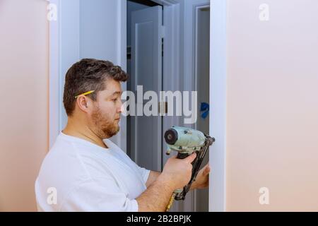 Le handyman de construction travaille à la rénovation de l'appartement à l'aide d'un pistolet à ongles d'air de moulage de porte Banque D'Images