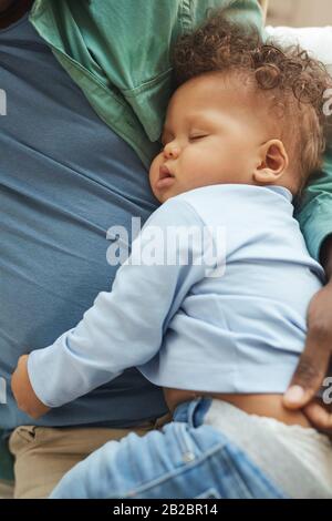 Au-dessus de la vue sur le mignon bébé de race mixte dormant dans les bras de pères Banque D'Images