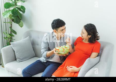 Un jeune couple heureux mangeant la salade ensemble au canapé dans le salon Banque D'Images