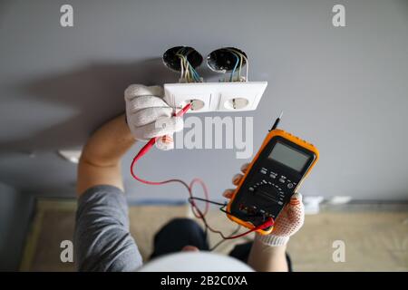 Homme dans un casque et des gants de protection vérifiant la prise wal avec testeur Banque D'Images