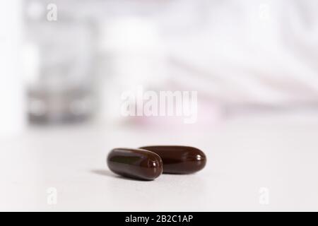 Pilules de vitamine sombre sur la table de chevet. Il y a un lit avec literie blanc neige, un verre d'eau en arrière-plan. Concept de médecine et de santé. Sélectif f Banque D'Images