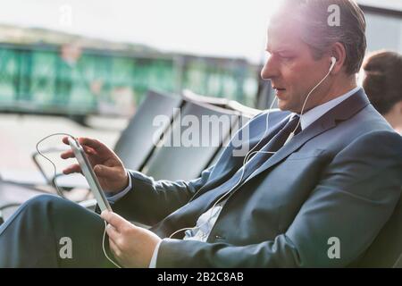 Portrait d'un homme d'affaires mûr utilisant une tablette numérique avec écouteurs en attente d'embarquement à l'aéroport Banque D'Images