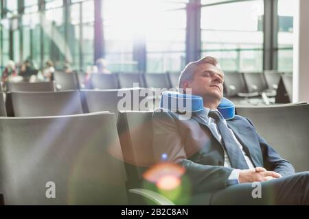 Homme d'affaires mûr assis et dormir avec son oreiller tout en attendant l'embarquement à l'aéroport Banque D'Images