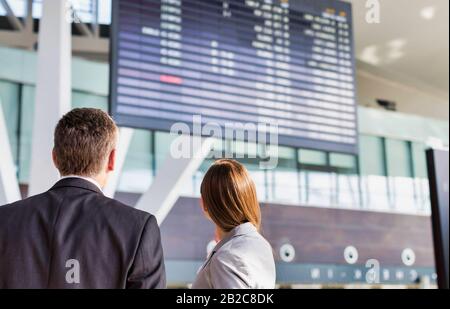 Les personnes en voyage d'affaires regardant sur l'écran d'affichage des vols à l'aéroport Banque D'Images