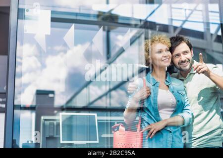 Photo d'un couple d'âge mûr regardant par la fenêtre de l'aéroport Banque D'Images