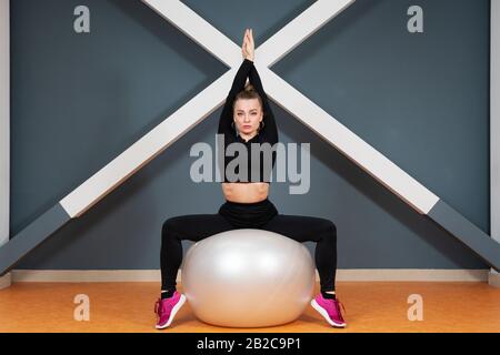 Belle femme est engagée dans la gymnastique assis sur un grand ballon de sport avec les mains vers le haut Banque D'Images