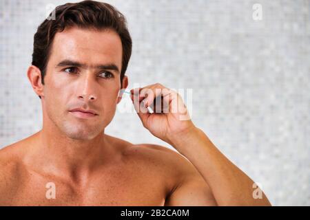 Portrait de jeune homme attrayant nettoyer ses oreilles avec des bourgeons de coton dans la salle de bains Banque D'Images