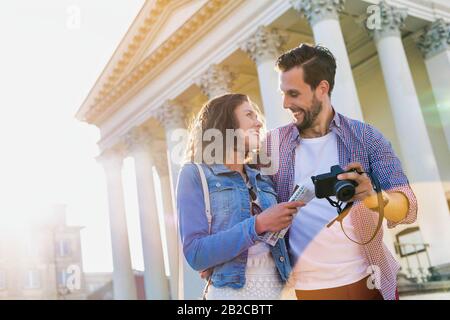Portrait de beau jeune homme montrant des photos sur l'appareil photo à sa belle petite amie tout en se tenant contre le musée avec l'éclat de lentille en arrière-plan Banque D'Images