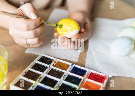 Jeune femme blonde peignant des œufs aux aquarelles pour la célébration de Pâques. Gros plan sur les mains Banque D'Images