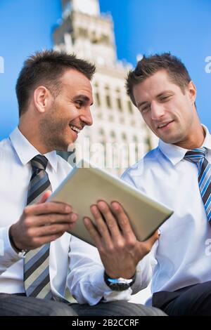 Portrait de bel homme d'affaires montrant plan d'affaires à l'autre homme d'affaires sur tablette numérique en étant assis