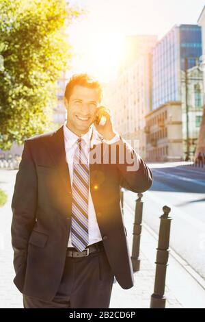 Portrait d'un homme d'affaires à la maturité et confiant souriant et parlant sur smartphone tout en marchant sur le pavé Banque D'Images