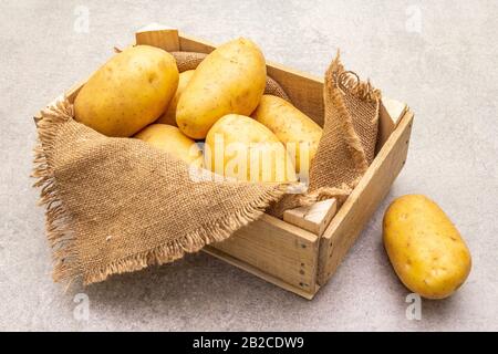 Dans une caisse en bois, les jeunes pommes de terre crues non pelées sont crues. Nouvelle récolte, sur toile de fond en pierre, gros plan Banque D'Images