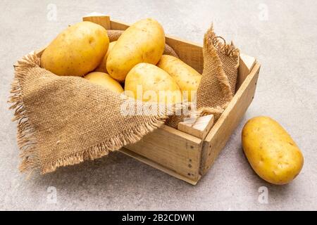Dans une caisse en bois, les jeunes pommes de terre crues non pelées sont crues. Nouvelle récolte, sur toile de fond en pierre, sur toile de fond, espace de copie Banque D'Images