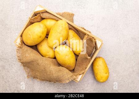 Dans une caisse en bois, les jeunes pommes de terre crues non pelées sont crues. Nouvelle récolte, sur toile de fond en pierre, vue de dessus Banque D'Images