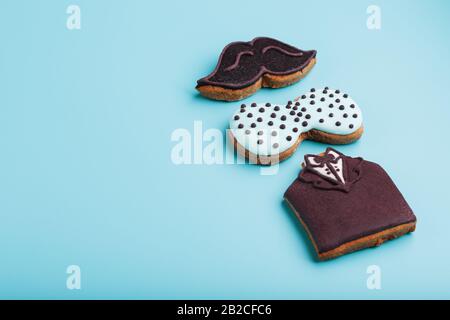 Pain d'épices glacé sous forme de moustache, papillon et smoking, pour homme sur fond bleu. Cookies faits main. Espace libre. Design minimaliste Banque D'Images