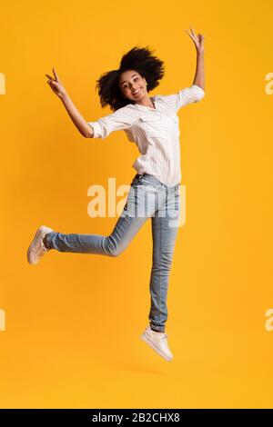 Happy Afro Girl Jumping Dans L'Air Et Gestuelle Signe De La Paix Banque D'Images