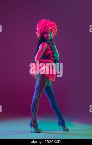 Fleurs. Modèle de brunette hawaïenne sur fond de studio mauve dans une lumière néon. Belles femmes dans des vêtements traditionnels souriant, dansant et s'amuser. Des vacances lumineuses, des couleurs de célébration, festival. Banque D'Images