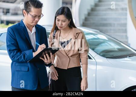 Réceptionniste asiatique qui vérifie la liste des entretiens avec le client au centre de service de maintenance pour dans le hall d'exposition Banque D'Images