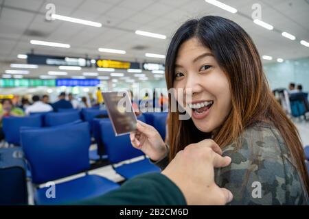 Main toucher sur l'épaule asiatique pour accueillir un ami à l'aéroport en attendant le vol à bord, main tenant passeport avec grand bagage, voyageur Banque D'Images