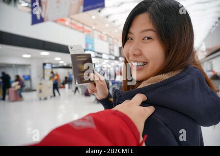 Main toucher sur l'épaule asiatique pour accueillir un ami à l'aéroport en attendant le vol à bord, main tenant passeport avec grand bagage, voyageur Banque D'Images