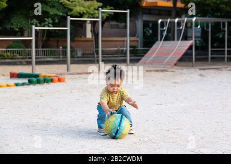 Jeu de bébé asiatique mignon avec ballon de football seul sur le terrain de jeu Banque D'Images