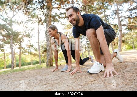 Photo d'un couple sportif heureux dans des vêtements de sport faisant des exercices tout en s'exerçant dans le parc vert pendant la journée ensoleillée d'été Banque D'Images