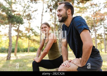 Photo de beau couple heureux dans les vêtements de sport faire des exercices tout en s'exerçant dans le parc vert pendant la journée ensoleillée d'été Banque D'Images