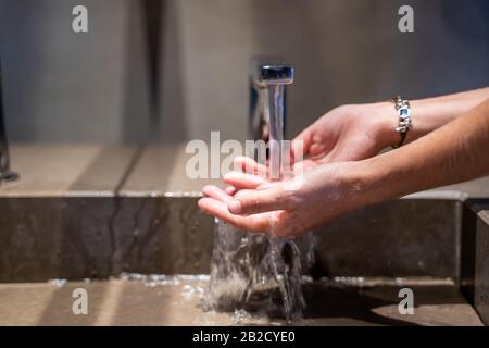 Mains d'une fille avec un anneau de lavage dans un évier d'une salle de bains avec de l'eau sortant Banque D'Images