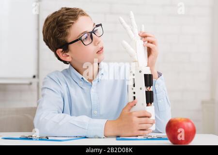 Un écolier concentré testant une nouvelle main robotique en classe Banque D'Images