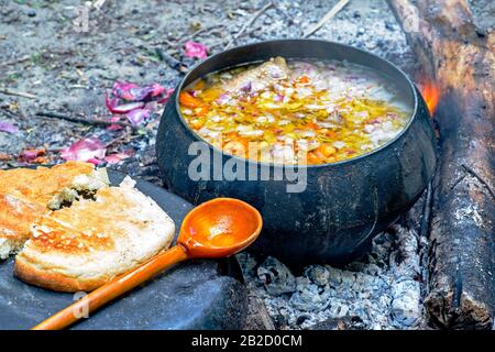 Le plat prêt à l'emploi est cuit dans une poêle ancienne sur les coals d'un feu avec une cuillère en bois et du pain blanc au premier plan. Aiguiser la cuillère. Le c Banque D'Images