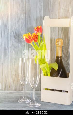 Une bouteille de champagne dans une boîte en bois. À côté de 2 verres de champagne et de fleurs de tulipes. Les vacances sont le 8 mars, fête des mères. Cadre romantique Banque D'Images