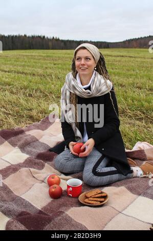 Syktyvkar, Russie - septembre 2019: Une belle fille d'apparence européenne avec de longs verrous boit du thé et semble pensivement dans la distance. Pique-nique dans la nature. Photographie d'automne. Banque D'Images