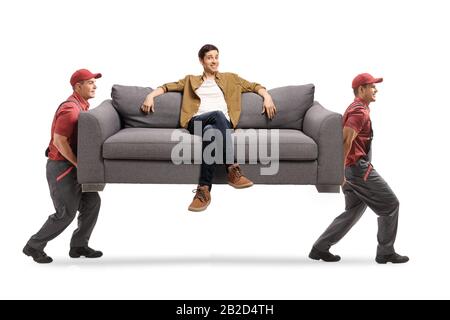 Deux travailleurs d'une entreprise de déménagement portant un canapé avec un jeune homme assis isolé sur fond blanc Banque D'Images