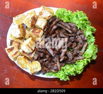 Portion de viande grillée sur la plaque avec sauce au persil et pain. Plat de restaurant. Photo isolée sur fond noir. Banque D'Images