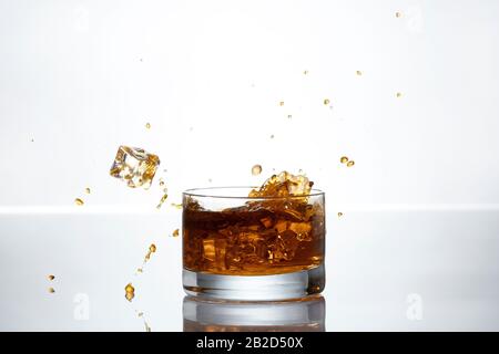 Un cube de glace s'éclabousse dans un verre de whisky Banque D'Images