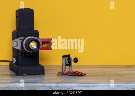 Gros plan d'un ancien projecteur noir en cours d'exécution pour regarder des diapositives et des bandes de film et un dispositif de serrage pour cadrer les images de diapositives sur une table. Bac jaune Banque D'Images