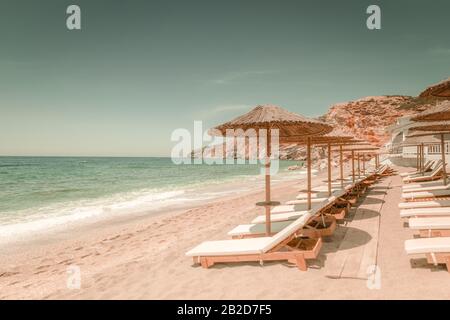 Magnifique plage de sable avec chaises pour la détente et parasols le jour ensoleillé. Île de Milos sur la mer Égée. Grèce. Vacances dans le concept de paradis Banque D'Images