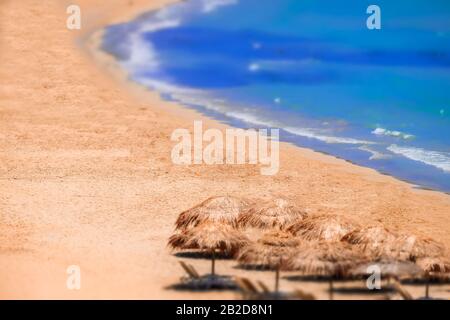 Flou de l'objectif inclinable. Vue abstraite sur un paysage de plage incroyable avec un parasol près de la mer d'Azure. Paradis méditerranéen en Grèce. Arrière-plan de voyage Banque D'Images