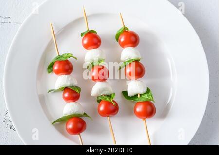 Brochettes de salade Caprese sur plaque blanche : vue du dessus Banque D'Images