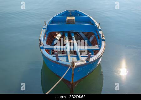 Аn bateau bleu en bois vide seul sur l'eau calme liée au port par une corde. Soleil sur l'eau bleue. Banque D'Images