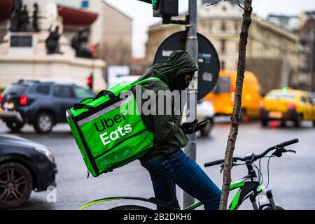 Jeune homme sur un vélo avec le logo Uber Eats fournissant de la nourriture pendant une journée de pluie à Bucarest, Roumanie, 2020 Banque D'Images