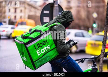 Jeune homme sur un vélo avec le logo Uber Eats fournissant de la nourriture pendant une journée de pluie à Bucarest, Roumanie, 2020 Banque D'Images