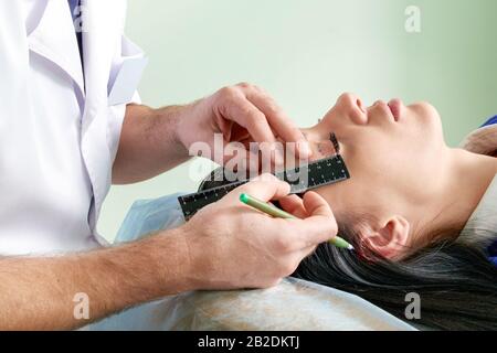 chirurgien de plastique et jeune femme avec des lignes de correction avant la chirurgie cosmétique, dessiner des lignes sur les yeux Banque D'Images