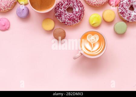 Deux tasses à café, délicieux beignets roses avec saupoudrez et macarons colorés sur fond de papier rose Banque D'Images