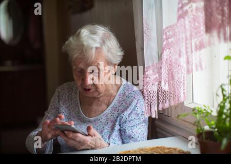 Une vieille femme avec un smartphone entre ses mains. Banque D'Images