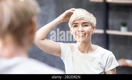 Femme D'Âge Moyen Touchant Cheveux Smiling Debout Dans La Salle De Bains, Panorama Banque D'Images