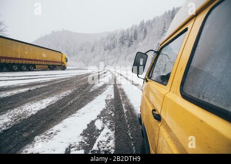 Carpathians, Ukraine - décembre 2019: Camionnette de camping-cars jaune conduite sur la route enneigée de terre avec forêt d'hiver sur fond. Banque D'Images