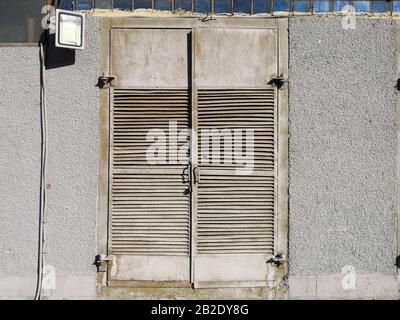 Vue de l'ancienne porte en métal gris à double feuille d'un panneau électrique dans le mur en béton d'un bâtiment industriel. Près du mur se trouve un spot électrique Banque D'Images