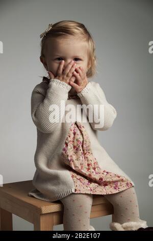 petite fille excitée couvrant sa bouche avec des palmiers sur fond gris Banque D'Images